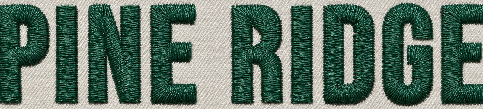 Makro-Fotoillustration der Stiche von Qepe für die Worte PINE RIDGE: eine Satinsäule für jeden Strich jedes Buchstabens, in dunkelgrünem Garn auf grauem Fleece